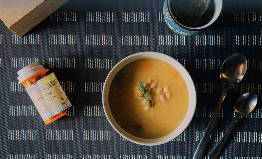 Bowl of soup next to a bottle of medicine on a table.